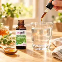 Pipette compte-gouttes versant de la teinture de propolis verte bio Propolia dans un verre d'eau le matin